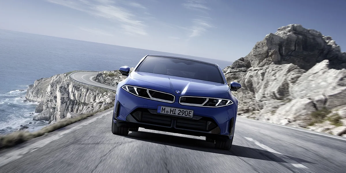 2027 BMW i3 electric sedan driving on a coastal road showing front design and performance stance.
