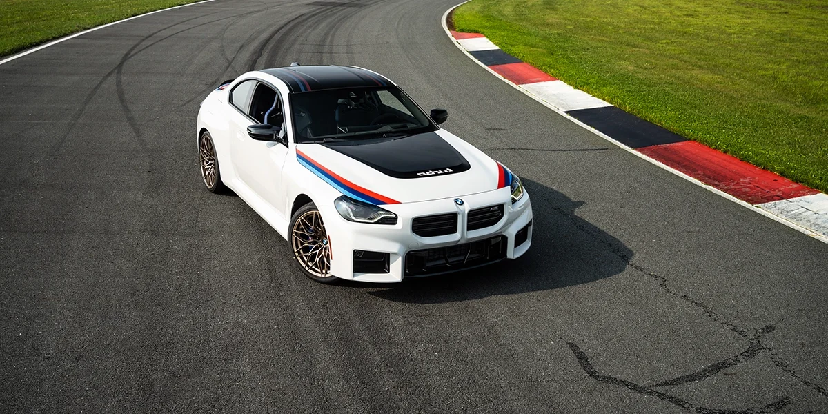 2026 BMW M2 Turbo driving on racetrack showcasing aerodynamic design and carbon-fiber hood.