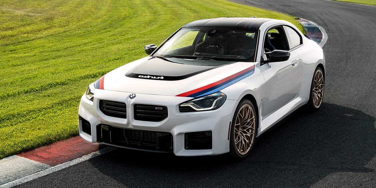 2026 BMW M2 Turbo on track cornering with M Motorsport stripes and gold alloy wheels.