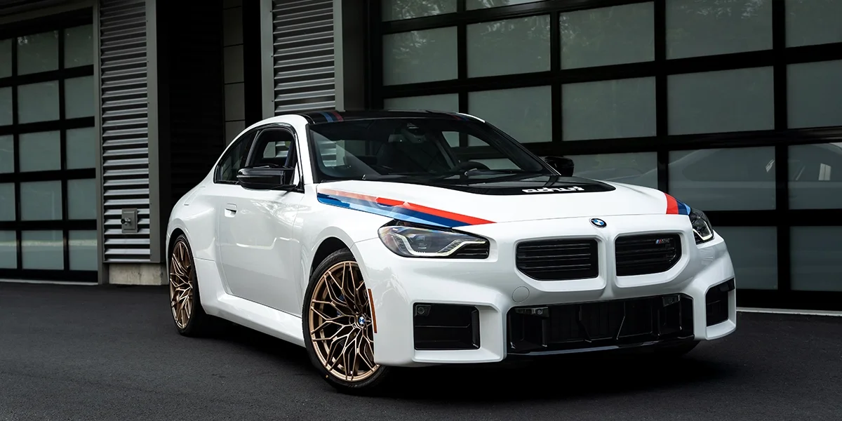 BMW M2 Turbo parked outside modern garage showing front-end styling, M colors, and performance stance.