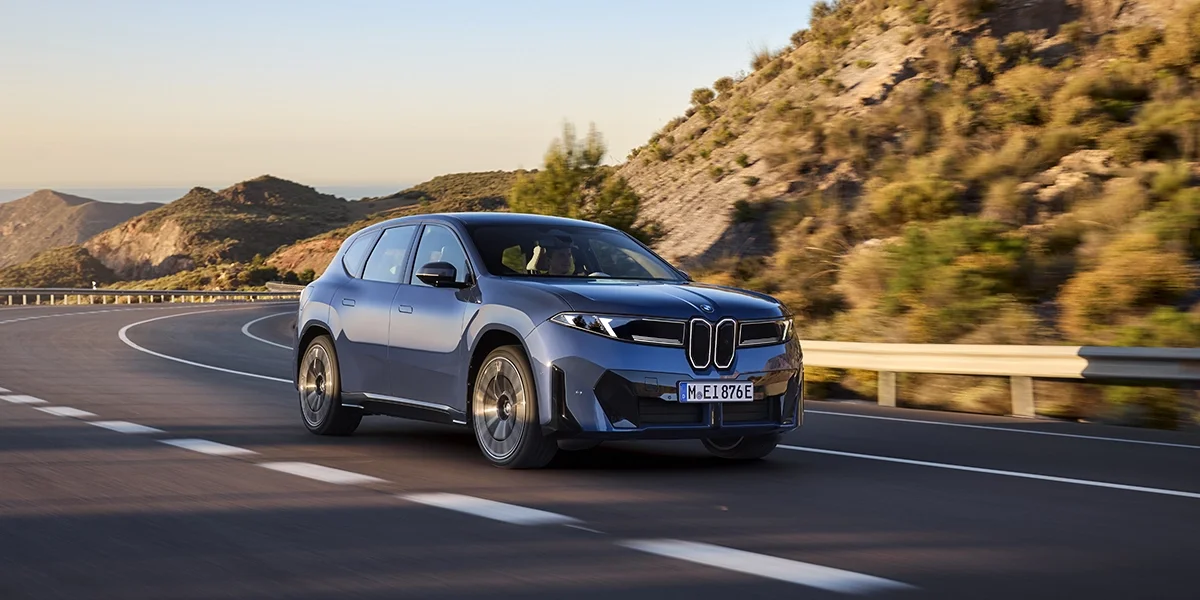 BMW iX3 50 xDrive side view on a rocky cliffside under blue skies.