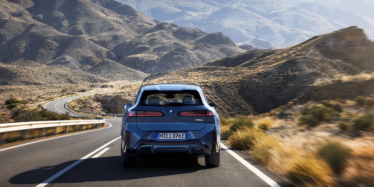Rear view of the BMW iX3 50 xDrive on a winding mountain road.