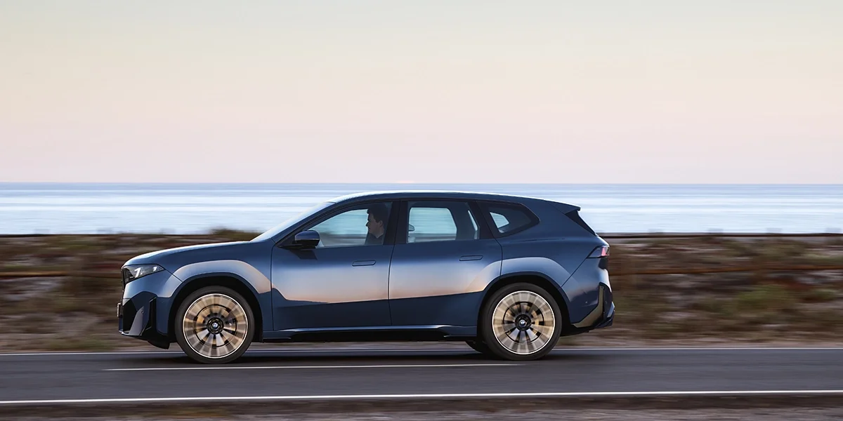 BMW iX3 50 xDrive driving side profile along a coastal highway.
