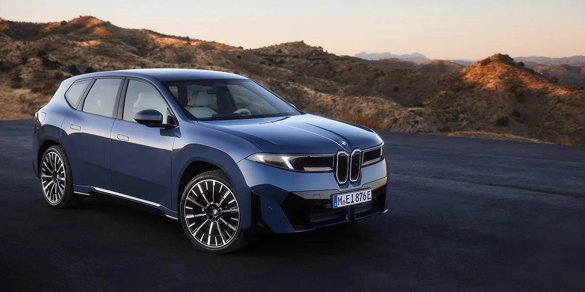 BMW iX3 50 xDrive in blue, front three-quarter view on a mountain road at sunset.