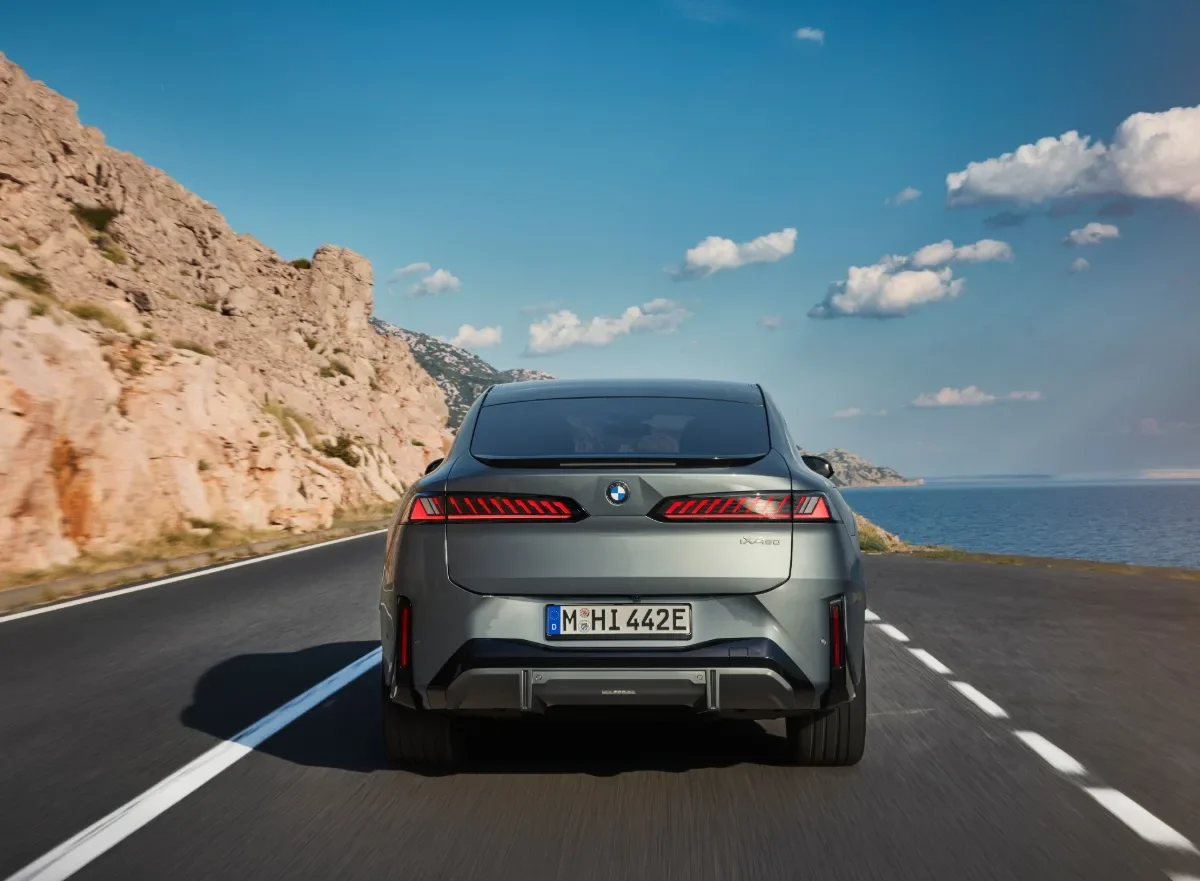 Rear view of a gray BMW iX4 50 xDrive on a coastal highway.